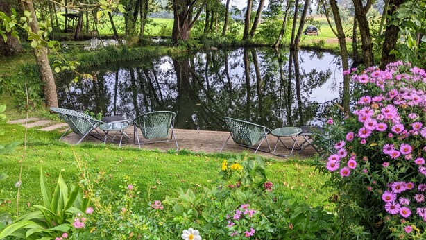 Un giardino tranquillo con uno stagno, sedie e fiori in fiore.