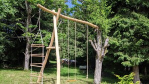 Un’altalena in legno con una scala, situata in una zona erbosa con alberi.