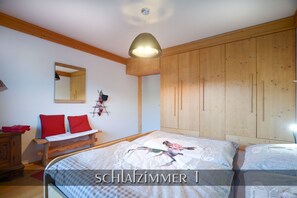 A bedroom with a wooden wardrobe, a bed with floral bedding, and a hanging light fixture.