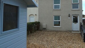 A two-story building with a white door and windows, a gravel driveway, and a small hedge. - Dog Friendly, Cosy Fisherman's Cottage Within 150 Metres Of A Long Sandy Beach  (Caister-on-Sea)