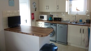 A compact kitchen with a washing machine, microwave, and a small island with a sink. - Dog Friendly, Cosy Fisherman's Cottage Within 150 Metres Of A Long Sandy Beach  (Caister-on-Sea)