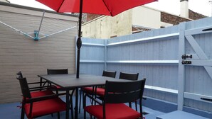 A patio with a table and chairs, a red umbrella, and a blue fence. - Dog Friendly, Cosy Fisherman's Cottage Within 150 Metres Of A Long Sandy Beach  (Caister-on-Sea)
