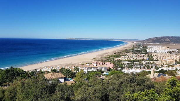 Un pueblo costero con playa, edificios residenciales y montañas al fondo.