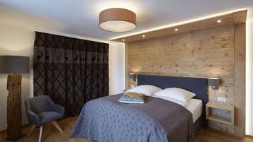 A modern bedroom with a wooden headboard, a bed with a patterned bedspread, a nightstand with a lamp, and a chair.