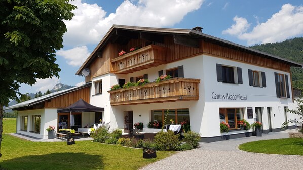 A two-story building with a balcony, a sign reading "Genuss-Akademie.tul", and a garden area with outdoor seating. - Alpine Chalet Vils in Tirol - on the Allgäu border - mountains, lakes, castles (Vils)