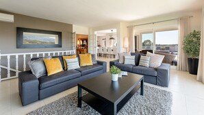 Ein modernes Wohnzimmer mit zwei dunklen Sofas, einem Couchtisch und einem großen Fenster mit Blick ins Freie.