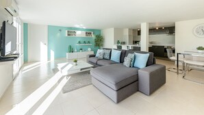 Ein modernes Wohnzimmer mit einem grauen Ecksofa, einem weißen Couchtisch und einer Küche im Hintergrund.
