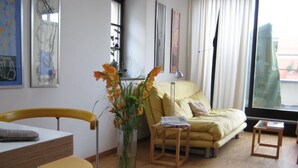 A modern living room with a yellow sofa, a wooden dining table, and a vase with flowers. - exclusive loft (Werder/Havel)