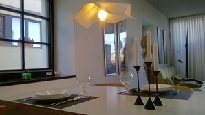 A dining area with a table set for two, a modern pendant light, and a view of the outside through large windows. - exclusive loft (Werder/Havel)