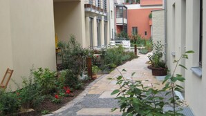 A narrow cobblestone pathway flanked by lush greenery and potted plants, leading to a row of residential buildings with balconies. - exclusive loft (Werder/Havel)