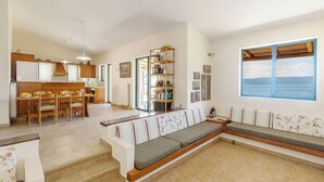 A spacious living area with a sofa, a dining table, and chairs. There is a staircase leading to an upper level.