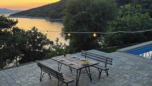A stone patio with a table and benches overlooking a body of water and hills.