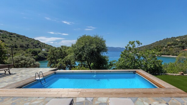 A rectangular pool with a wooden deck, stone tiles, and two lounge chairs.