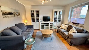 Een woonkamer met twee banken, een salontafel en een televisie op een kast. Er is een boekenkast en een raam met uitzicht.