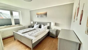 Een slaapkamer met een bed, nachtkastjes, een radiator, een raam en een kunstwerk aan de muur.