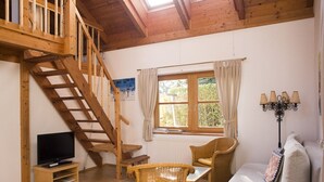 A cozy room with a wooden staircase, a television, wicker furniture, a window with curtains, and a lamp. - Organic home, garden & swimming pond, quiet location, Vienna reached in 15 min (Maria Enzersdorf)