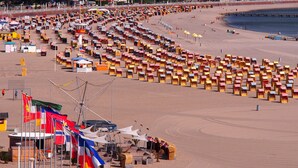 A beach with rows of beach huts and a flag display.