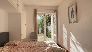 Quarto com cama, uma cadeira, guarda-roupa e janela com vista para o verde.