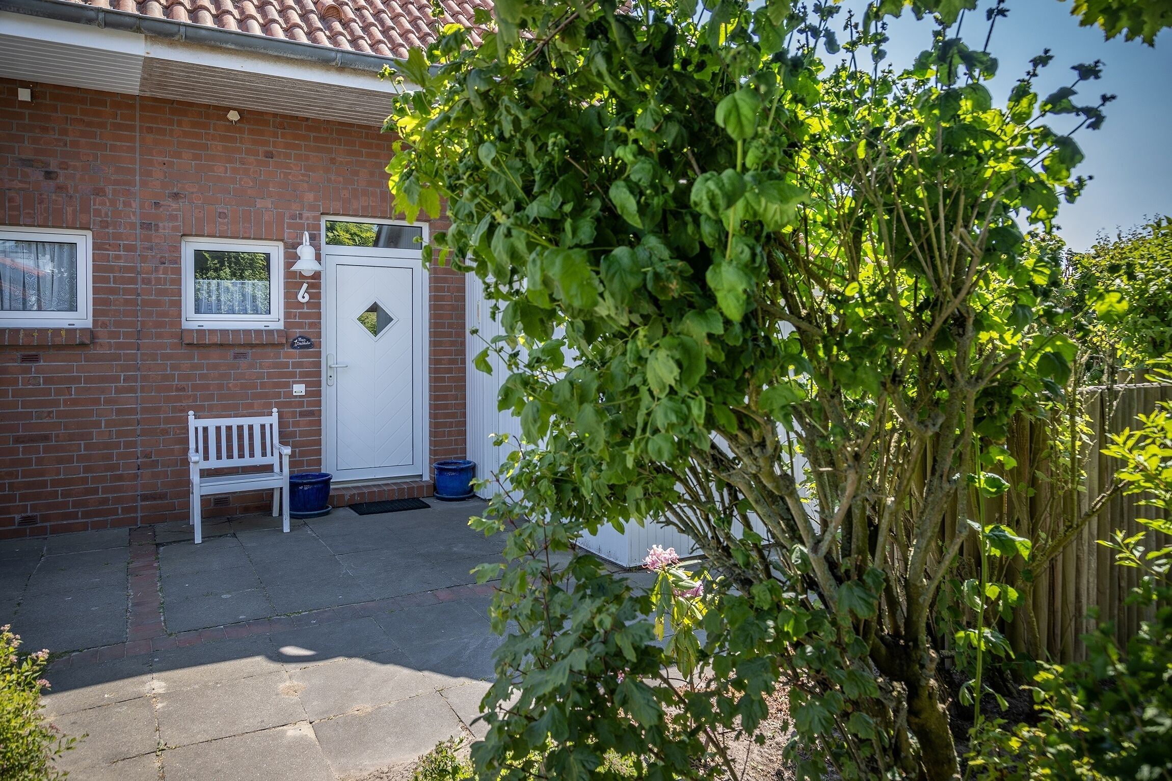 A brick house with a white door, a bench, and a blue bucket outside.