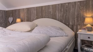 Een net opgemaakt bed met witte lakens, een houten hoofdbord en een nachtkastje met een lamp en een decoratief object.