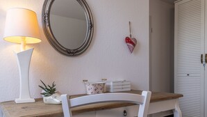 Een kamer met een houten bureau, een witte stoel, een spiegel, een lamp, een hartvormige decoratie en een witte garderobe.