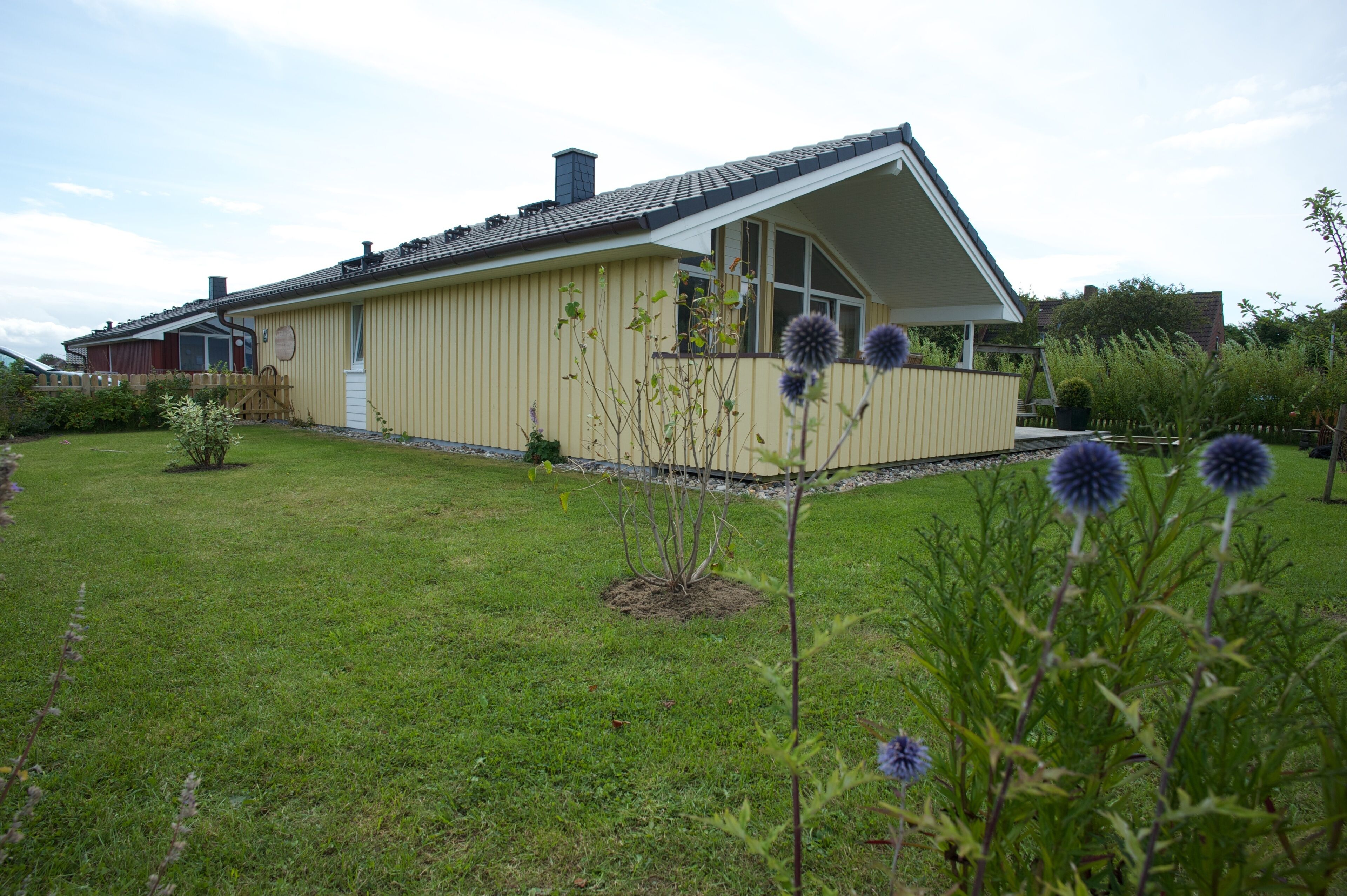A single-story yellow building with a sloped roof, a small porch, and a fenced yard.
