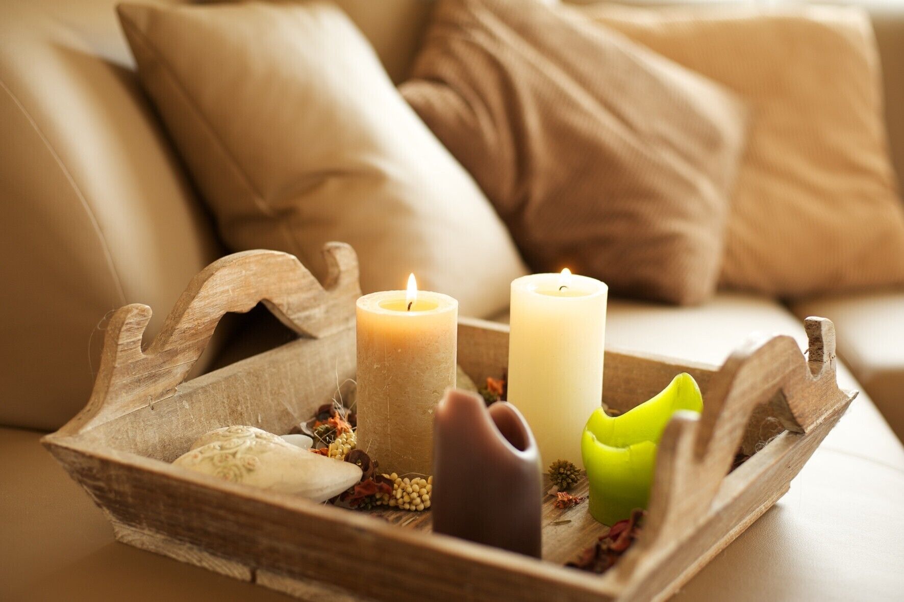 A wooden tray with candles and decorative items on a beige sofa.