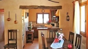 A dining area with a wooden table, chairs, and a rustic ceiling beam. A kitchen is visible in the background with a window and a clock. - WIFI Villa with garden and private pool, near the town and beaches. Pollença (Pollença)