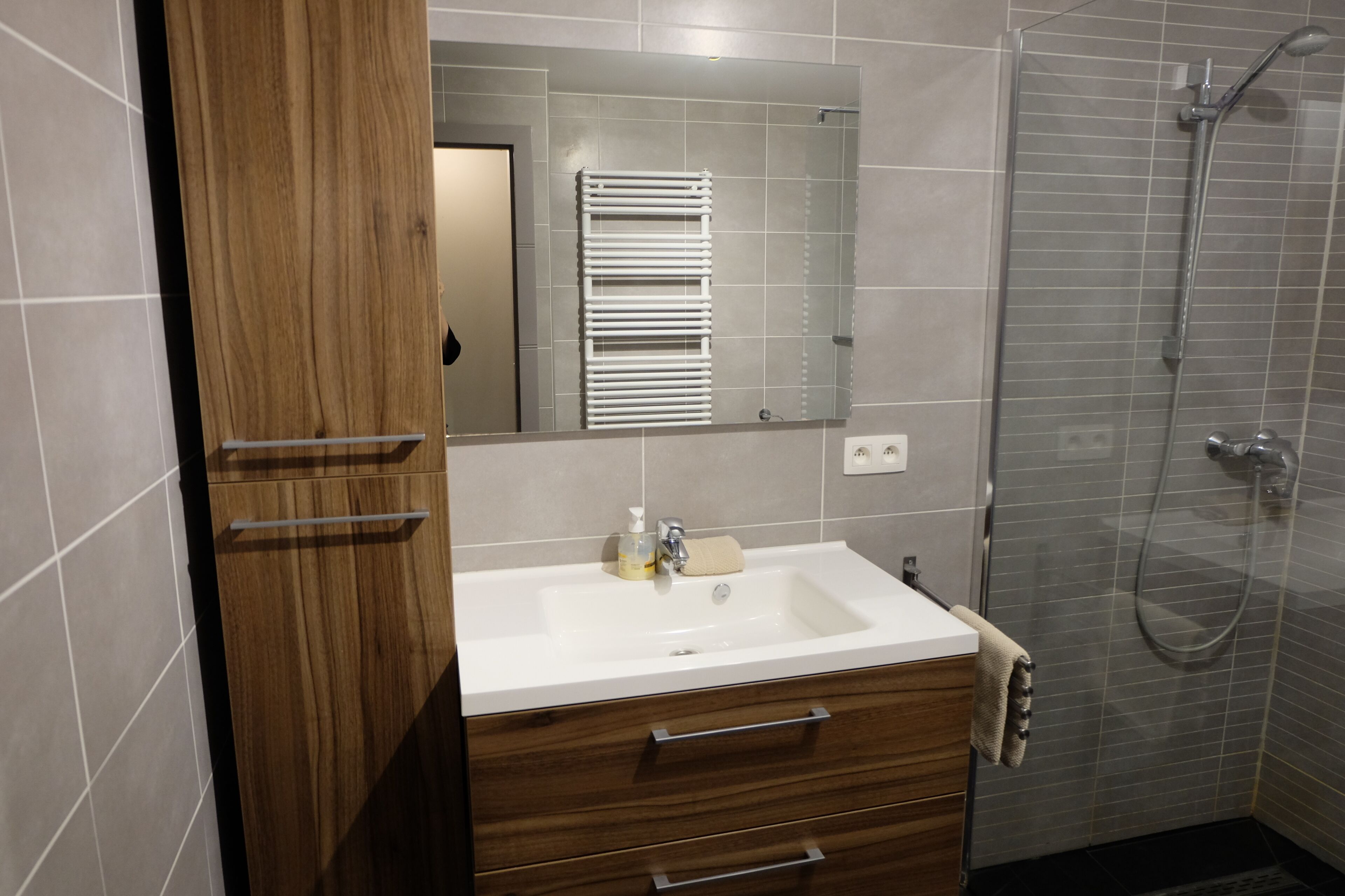A modern bathroom with a wooden vanity, a white sink, and a glass shower enclosure.