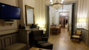 A living room with a television, a fireplace, a chandelier, and a dining area with a table and chairs. - Superb character duplex in the European district (Ixelles)