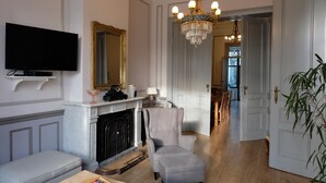 A living room with a television, fireplace, armchair, and chandelier. - Superb character duplex in the European district (Ixelles)