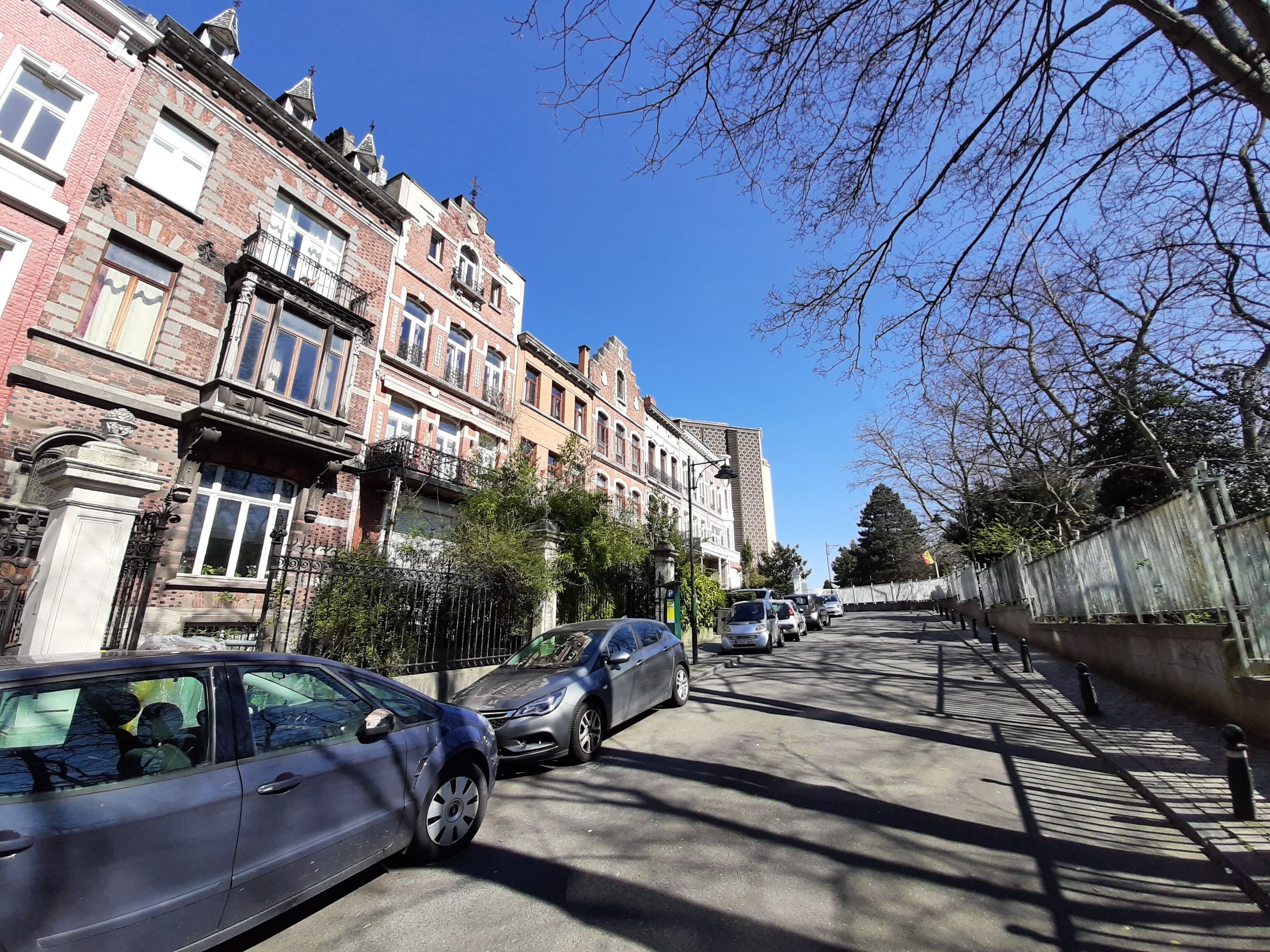 Una calle bordeada de edificios históricos de ladrillo, coches aparcados y un cielo azul despejado.