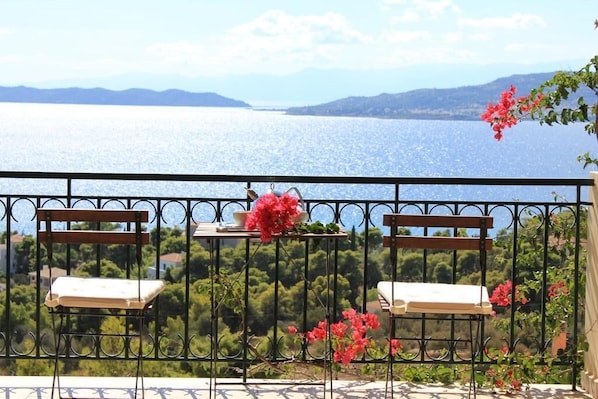 A balcony with two wooden chairs and a table, overlooking a body of water and greenery.