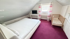 Une chambre avec un lit simple, un bureau avec un ordinateur, un berceau et une fenêtre avec des rideaux.