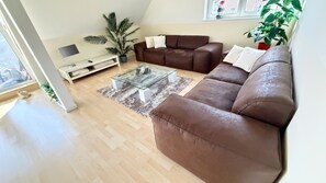 A modern living room with a brown leather sofa, a glass coffee table, and a white TV stand.