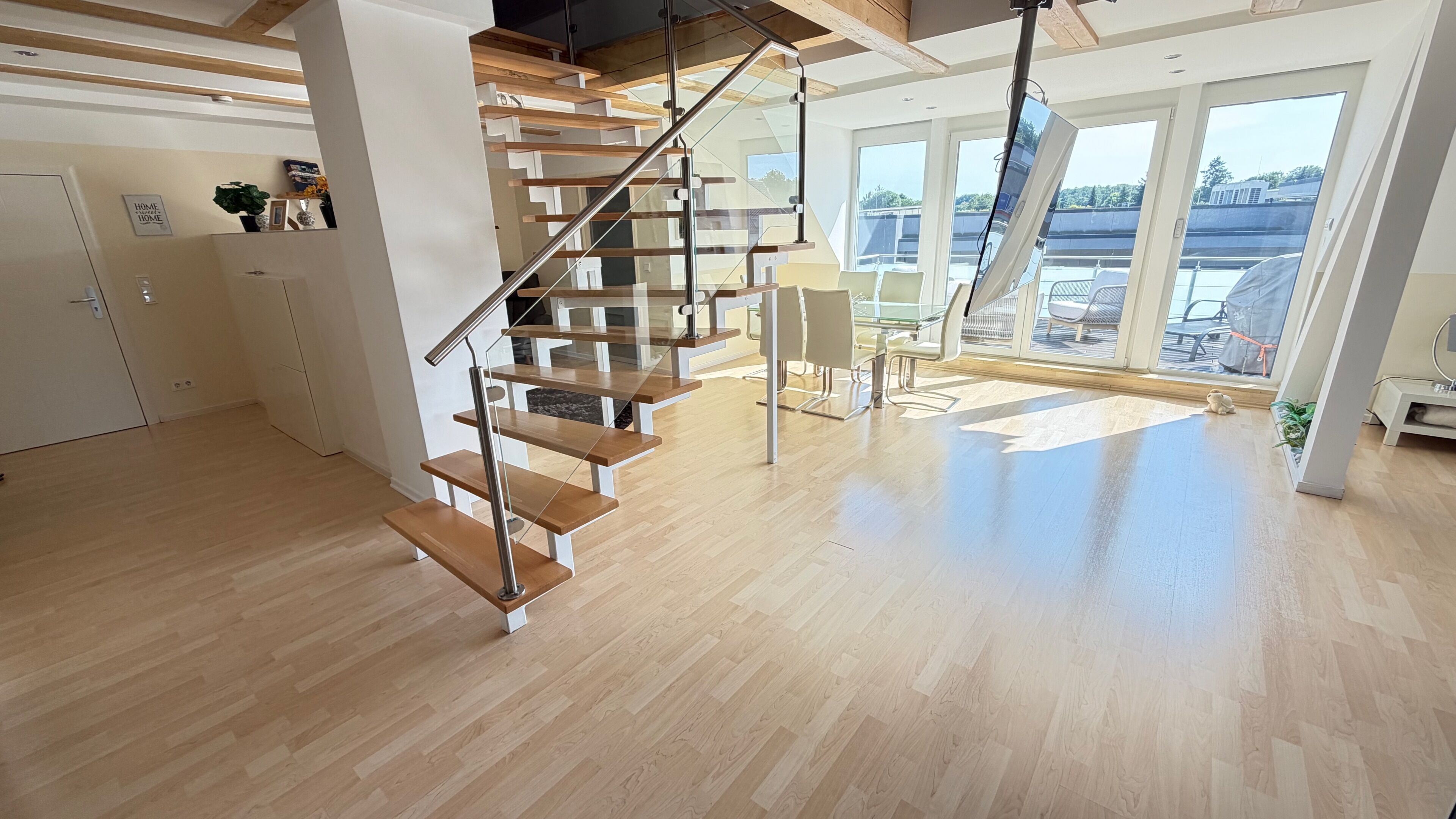Ein modernes Interieur mit einer Holztreppe, einem Essbereich und großen Fenstern mit Blick ins Freie.