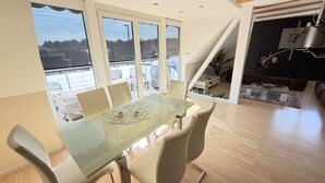 Comedor con mesa y sillas de vidrio, ventanas amplias y vistas al exterior.