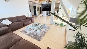 Una sala de estar moderna con un sofá de cuero marrón, una mesa de centro de vidrio y un televisor montado en una pared blanca.