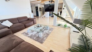 A modern living room with a brown leather sofa, a glass coffee table, and a TV mounted on a white wall.
