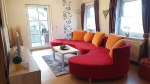 A living room with a red sofa, a white coffee table, and a large window with curtains. - Family-friendly apartment in the heart of East Frisia incl. Wireless Internet access (Westerholt)