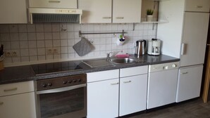 A kitchen with white cabinets, a stainless steel sink, a stove, and a coffee maker. - Family-friendly apartment in the heart of East Frisia incl. Wireless Internet access (Westerholt)