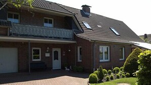 A two-story brick house with a front garage, a small porch, and a well-maintained lawn with trimmed bushes. - Family-friendly apartment in the heart of East Frisia incl. Wireless Internet access (Westerholt)