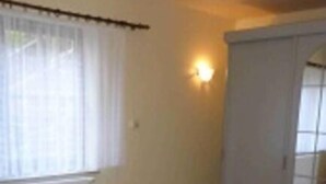 Een kamer met een enkel bed, raam, wandlamp en een radiator.