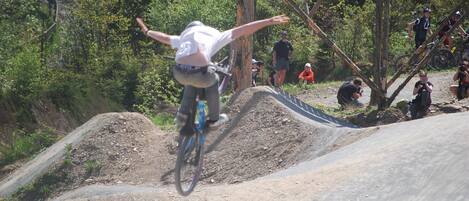 A person performing a BMX stunt on a dirt track with spectators and a photographer in the background.