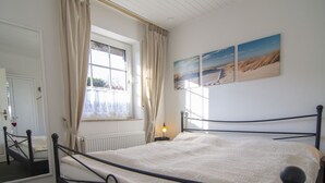 A bedroom with a bed, a window with curtains, a radiator, and wall art. - Modern, large 4 star house w/sauna and fireplace - 800m to the North Sea shore (Dornumersiel)