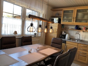 A kitchen with wooden cabinets, a dining table with chairs, and pendant lights. - Modern, large 4 star house w/sauna and fireplace - 800m to the North Sea shore (Dornumersiel)