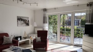 A modern living room with a red sofa, a white coffee table, and a red armchair. There is a large window with a view of the outside, a lamp, and a painting on the wall. - Modern, large 4 star house w/sauna and fireplace - 800m to the North Sea shore (Dornumersiel)