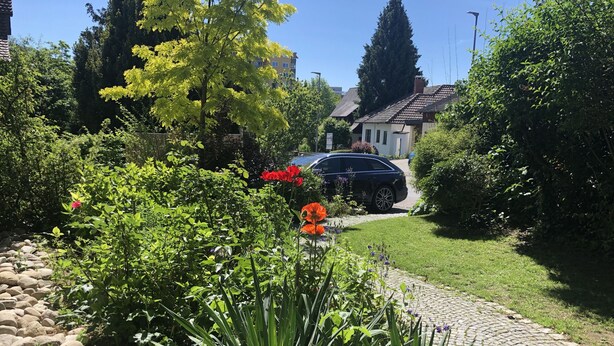 A residential garden with a cobblestone pathway, lush greenery, and a parked car. - Idyllic apartment, central near the lake (Überlingen)