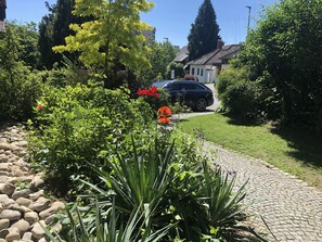 A residential garden with a cobblestone pathway, lush greenery, and a parked car. - Idyllic apartment, central near the lake (Überlingen)