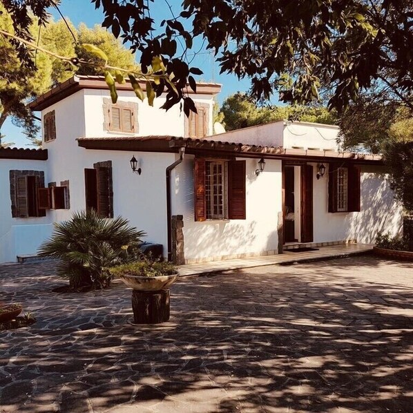 A white building with a tiled roof, wooden shutters, and a stone staircase leading to the entrance.